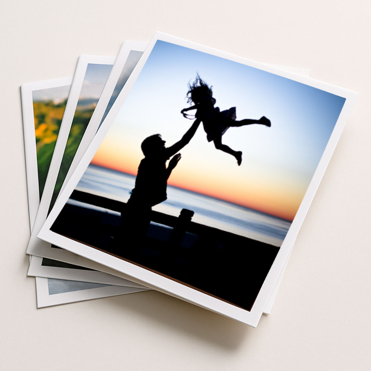 Stack of photo prints with a silhouette of a man and child at sunset on a beach.